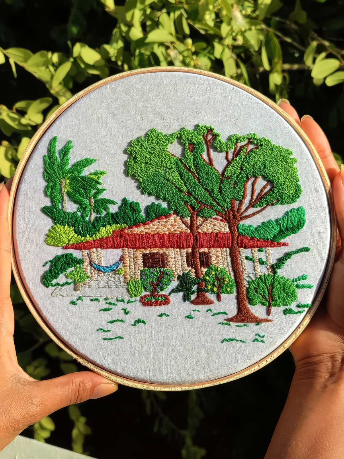 Bastidor com casa de telhado vermelho, rede e árvore bordadas em verde