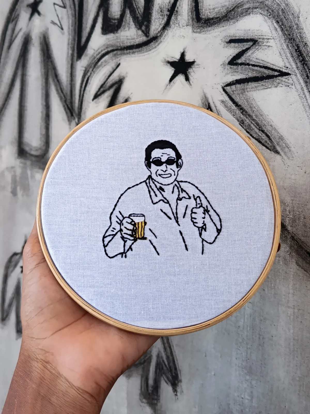Bastidor com retrato do Zeca Pagodinho segurando um copo, em linha preta